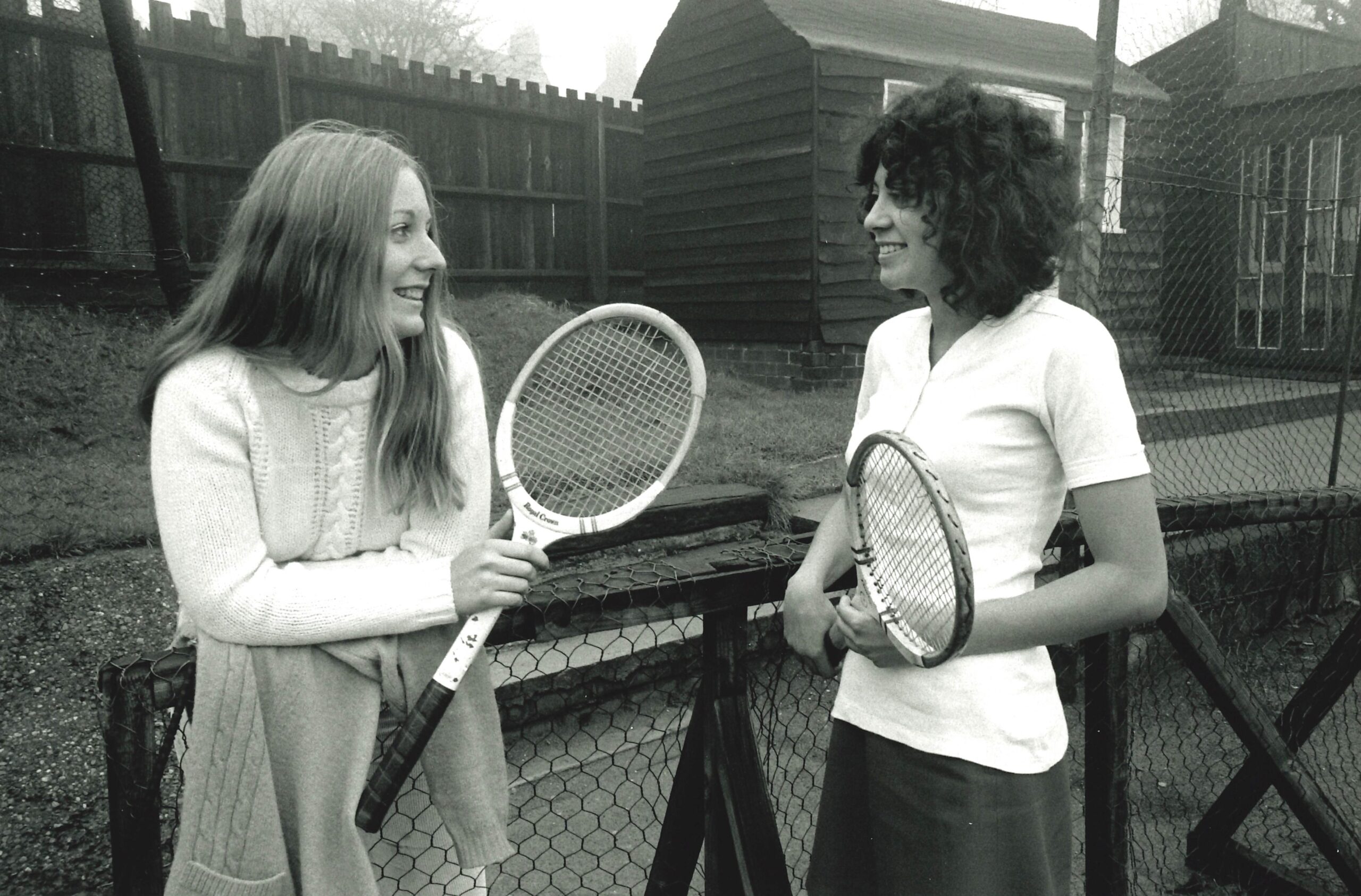 Two women standing near a tennis net, holding racquets