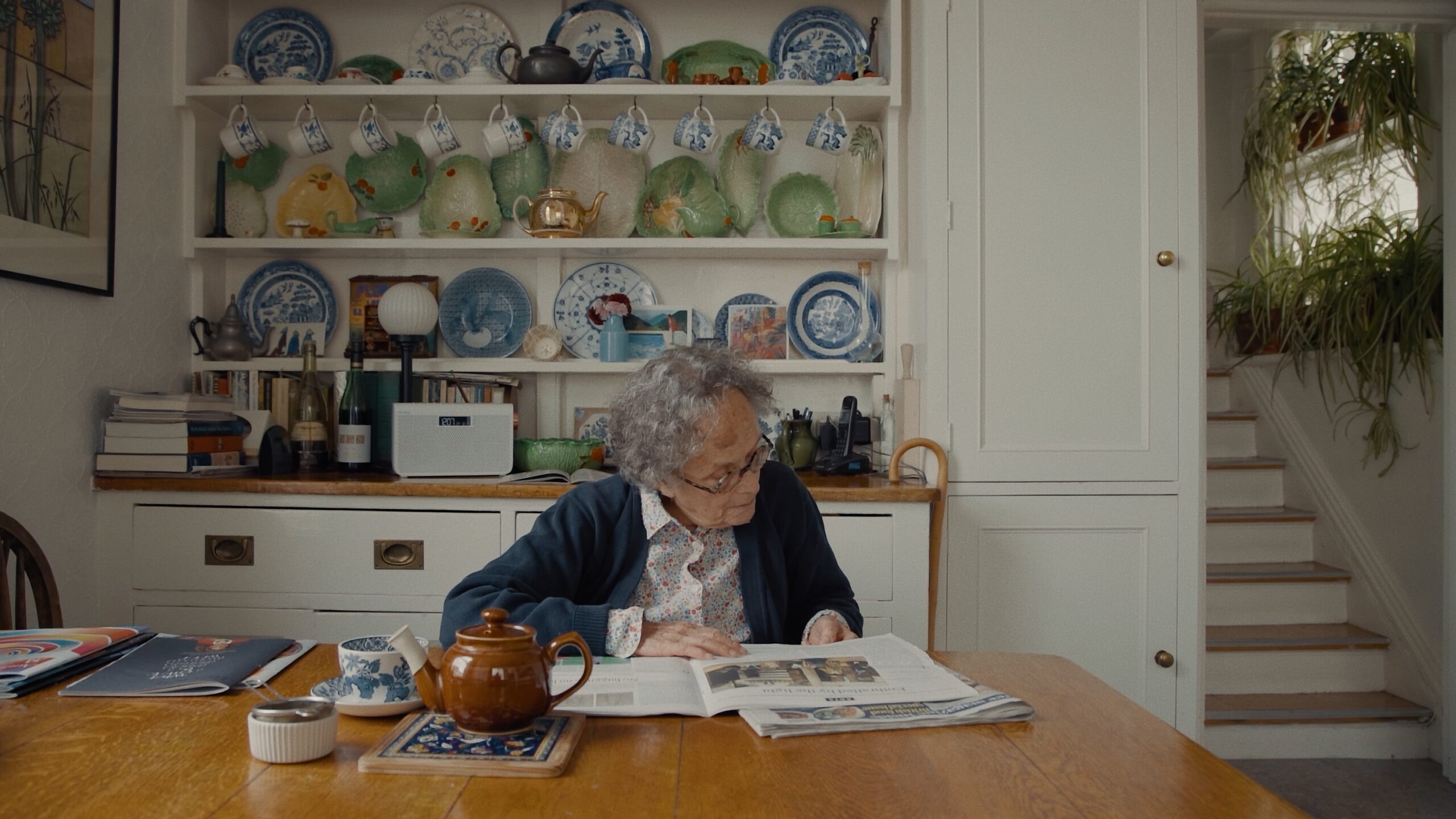 Ruth Fainlight sitting in her kitchen, reading.