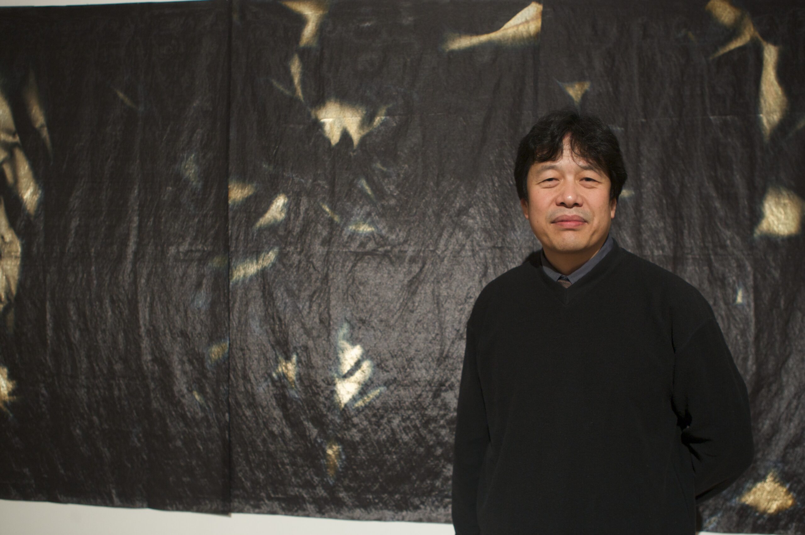 Dr. Kinor Jiang standing in front of a large black and gold tapestry.