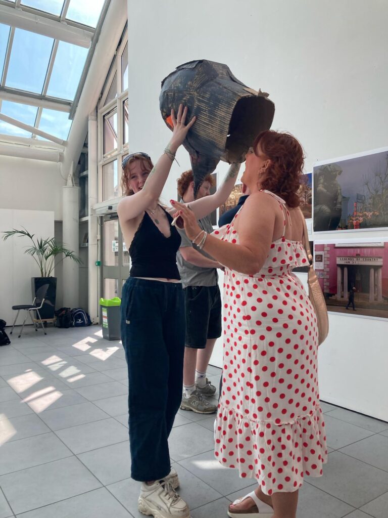 Two people having fun in a garment making and customisation workshop. They are playing with a cardboard mask of a birds head.