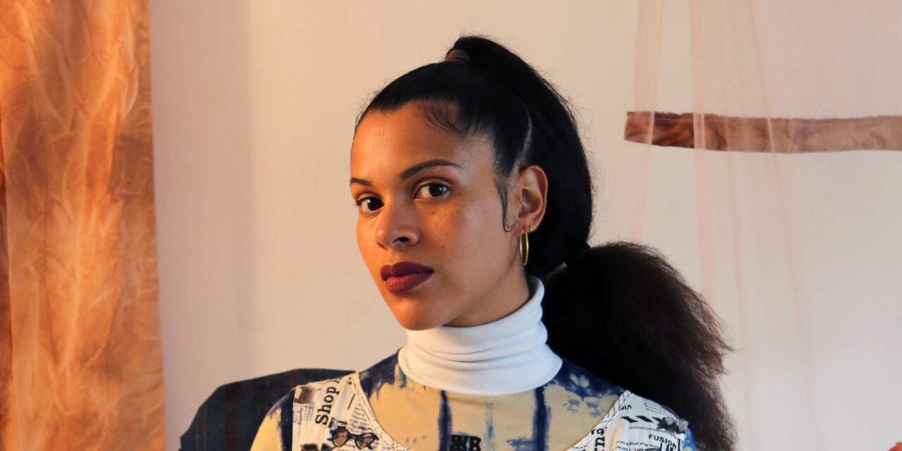 Portrait of Ibiye Camp wearing a white turtle neck layered under a patterned top.